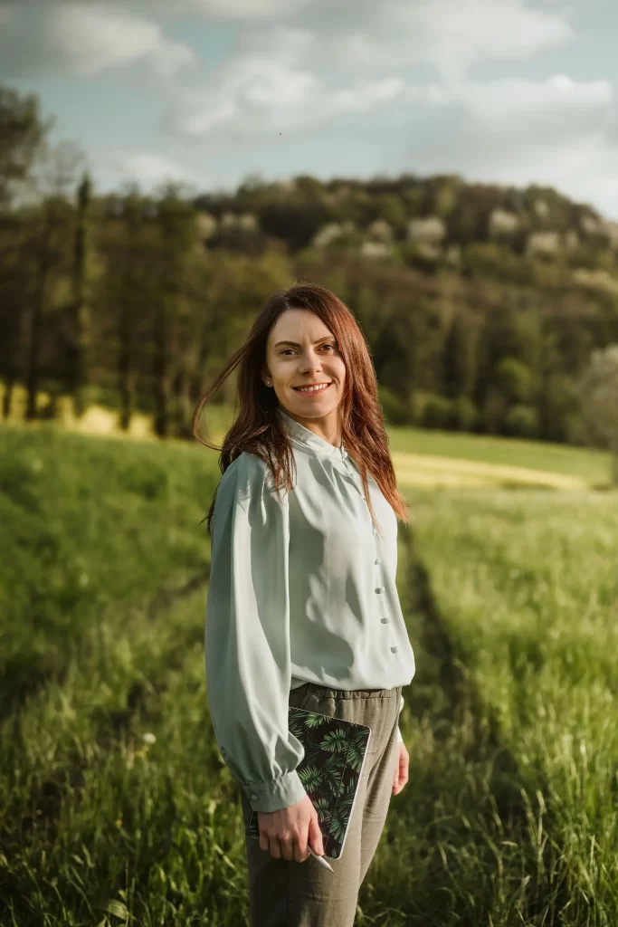 Donna con camicia verde in mezzo a un campo che guarda sorridente in camera