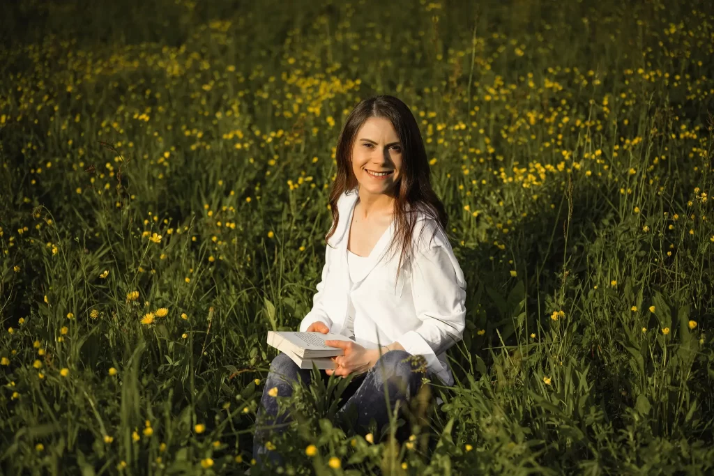 Donna con libro in un campo di fiori che guarda sorridente in camera